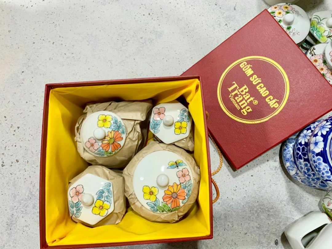 Hộp quà gốm sứ Bát Tràng thủ công men mờ trắng ngà trên nền vải linen, ruy băng hồng, ánh sáng tự nhiên ấm